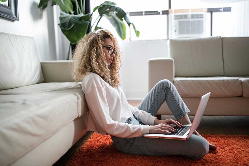 Woman working on laptop in bright living room.