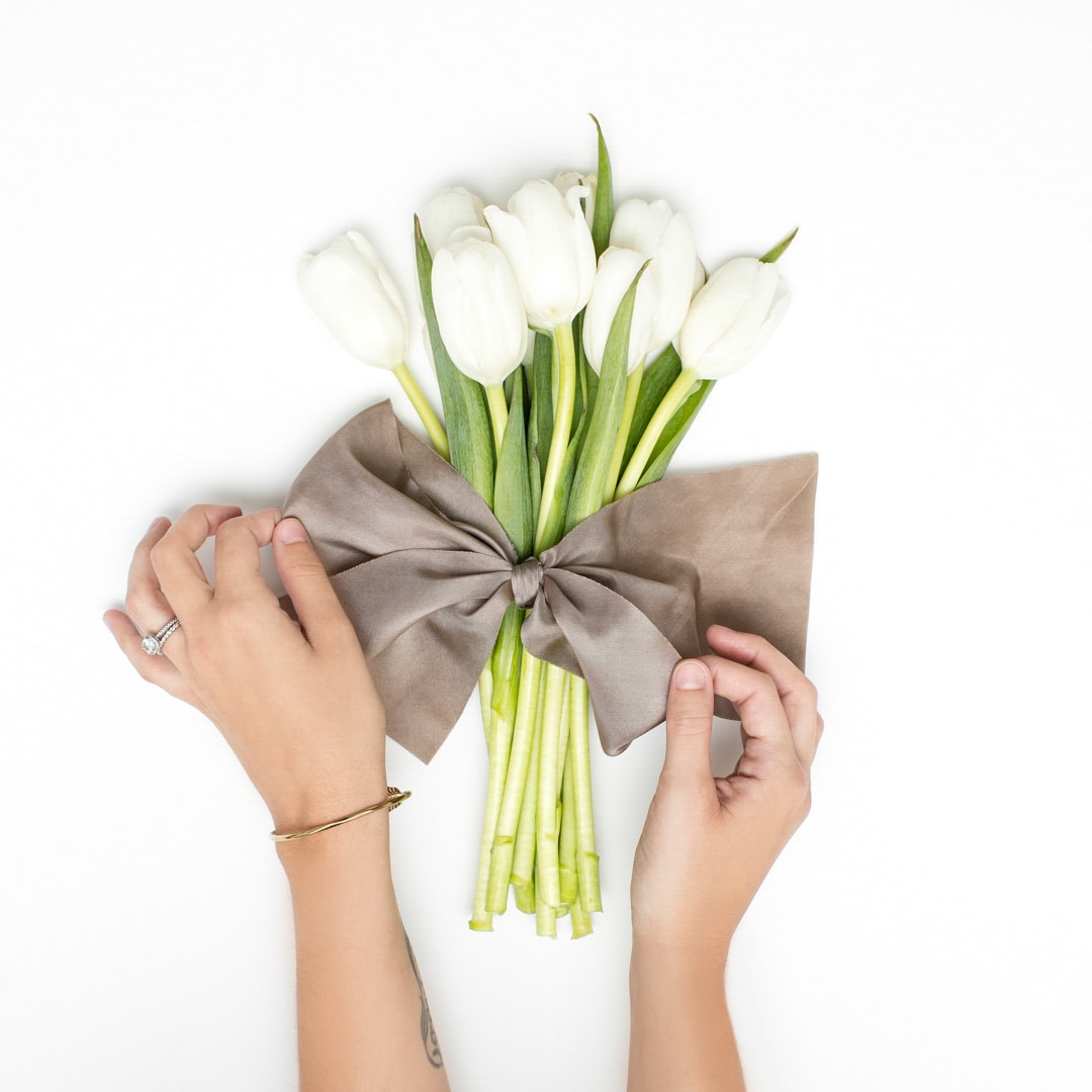 Hands tying ribbon on white tulips bouquet.