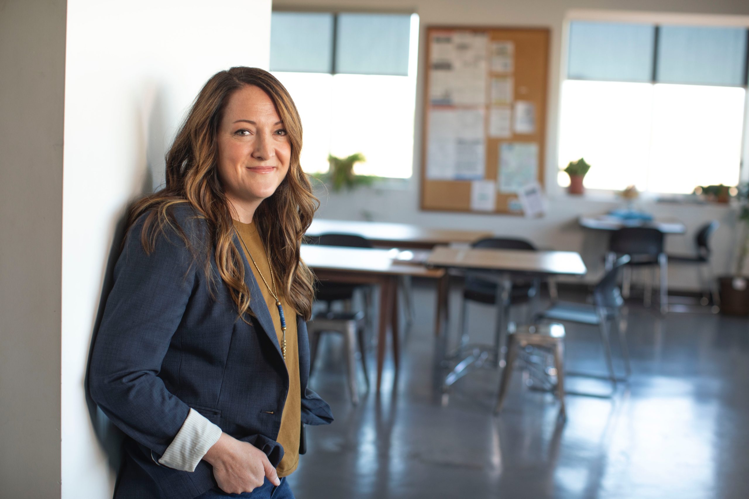 Smiling woman in office with bright windows and desks.