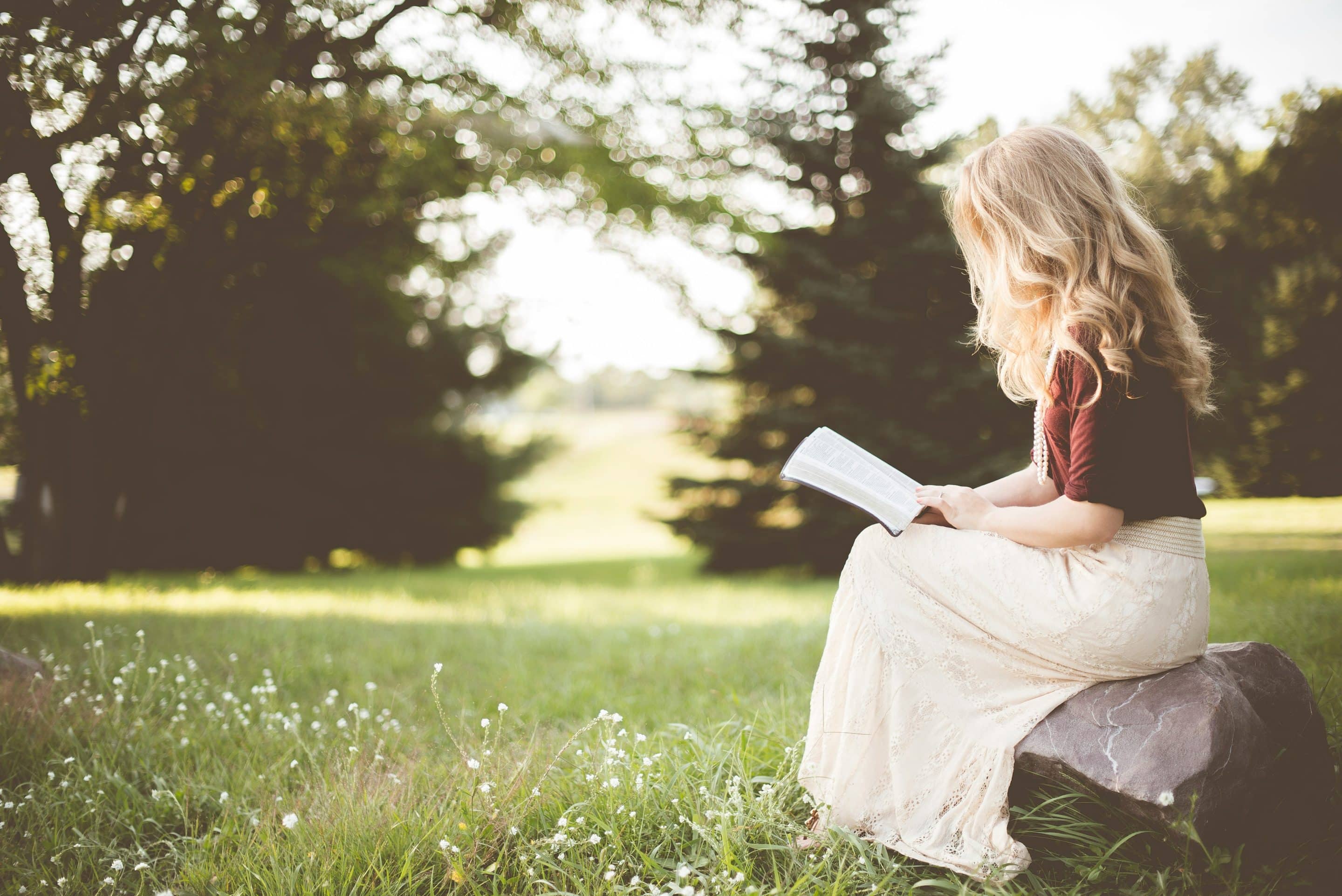 Woman reading book in peaceful outdoor setting.
