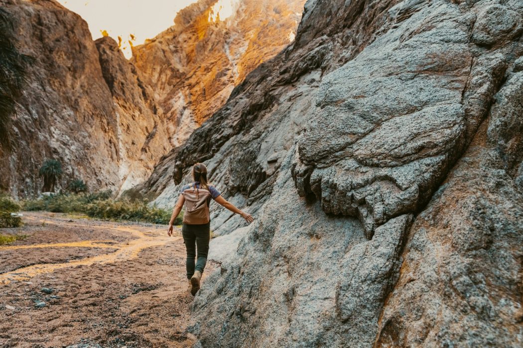 Hiker exploring rocky canyon trail at sunset.