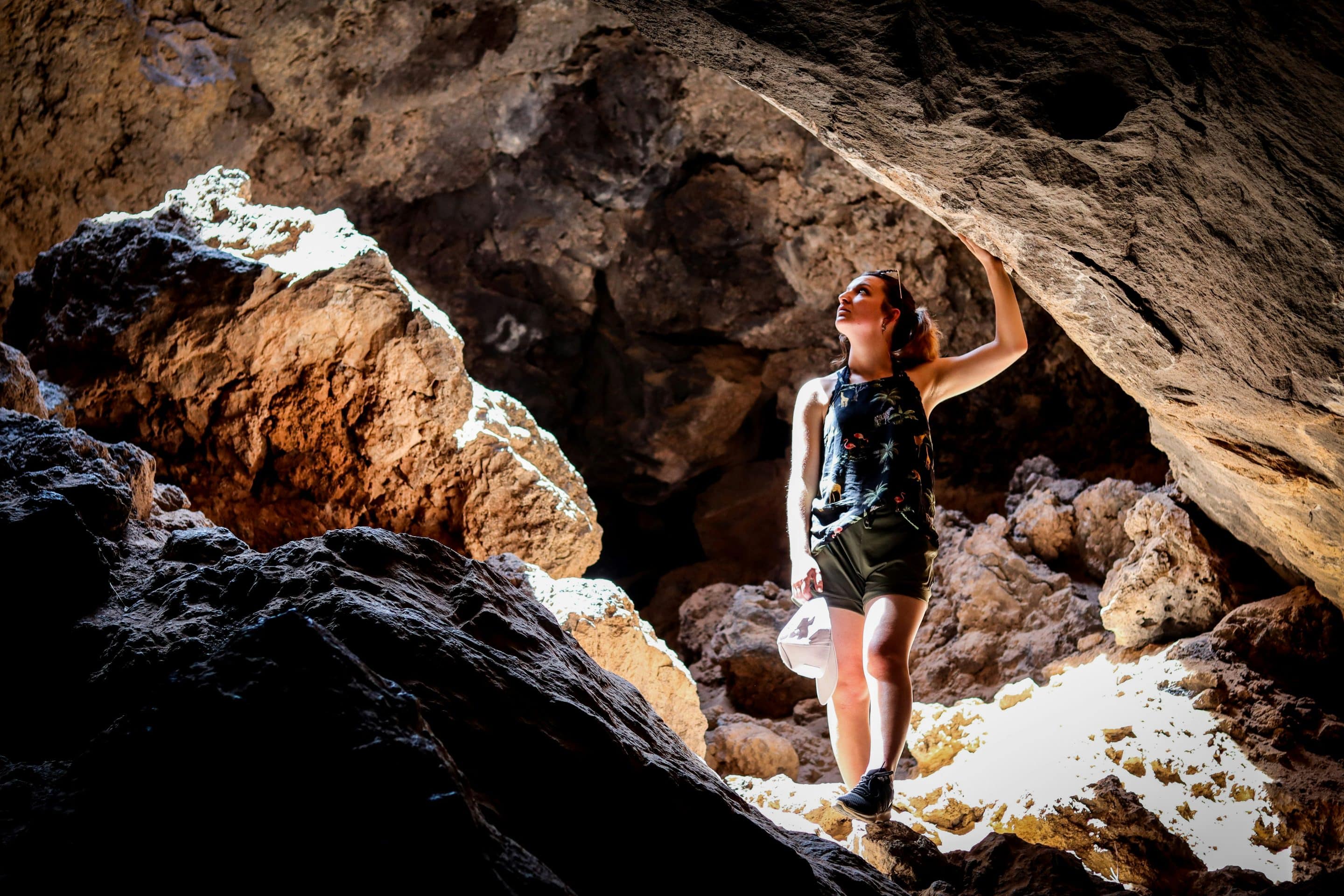 Woman exploring sunlit cave opening.