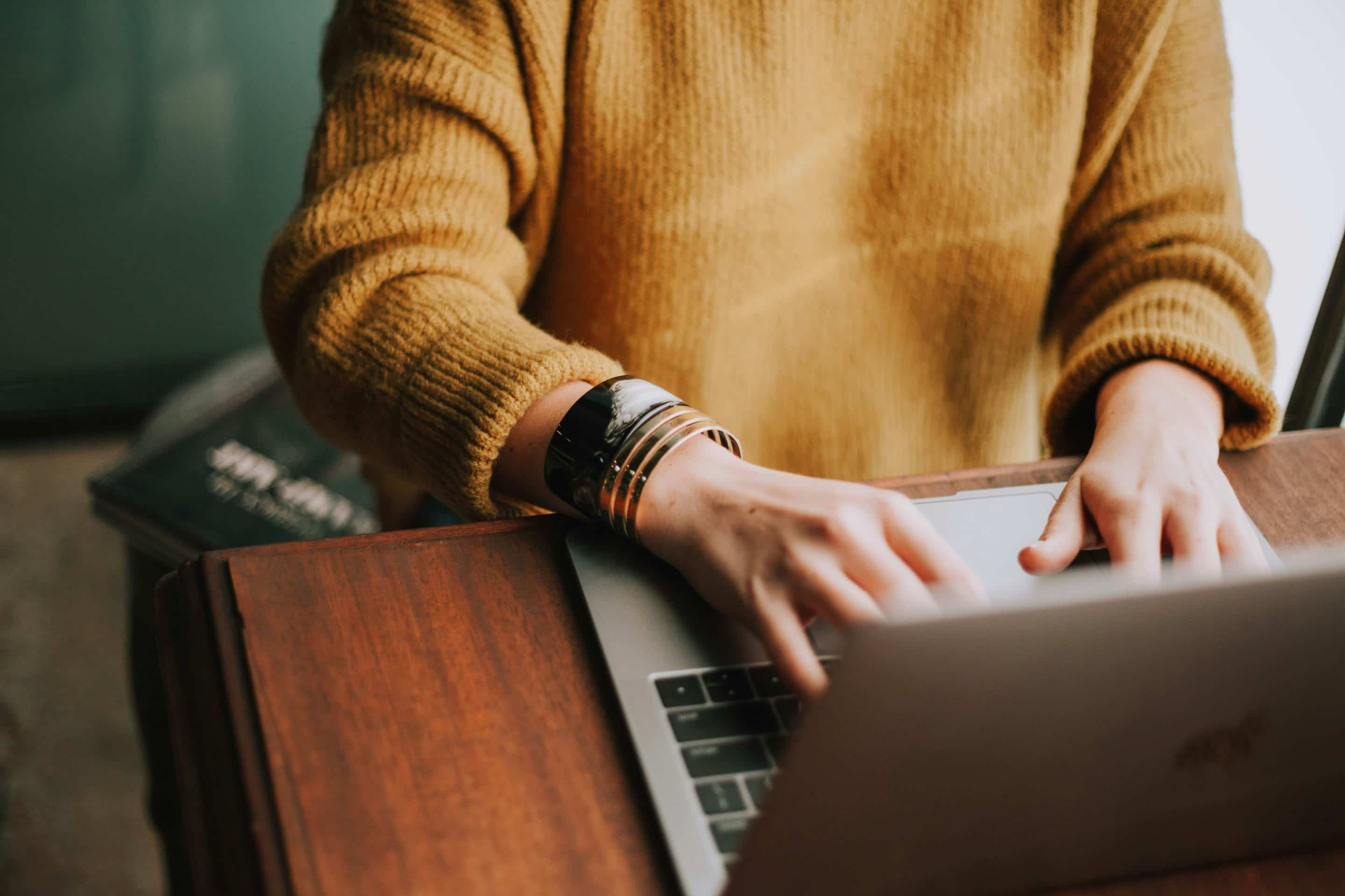 Person typing on laptop with books and wooden desk.