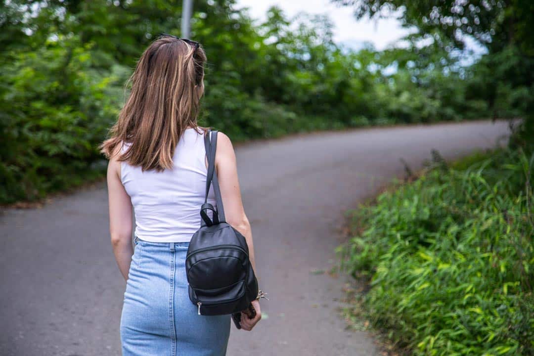 Woman walking on a leafy path with backpack.